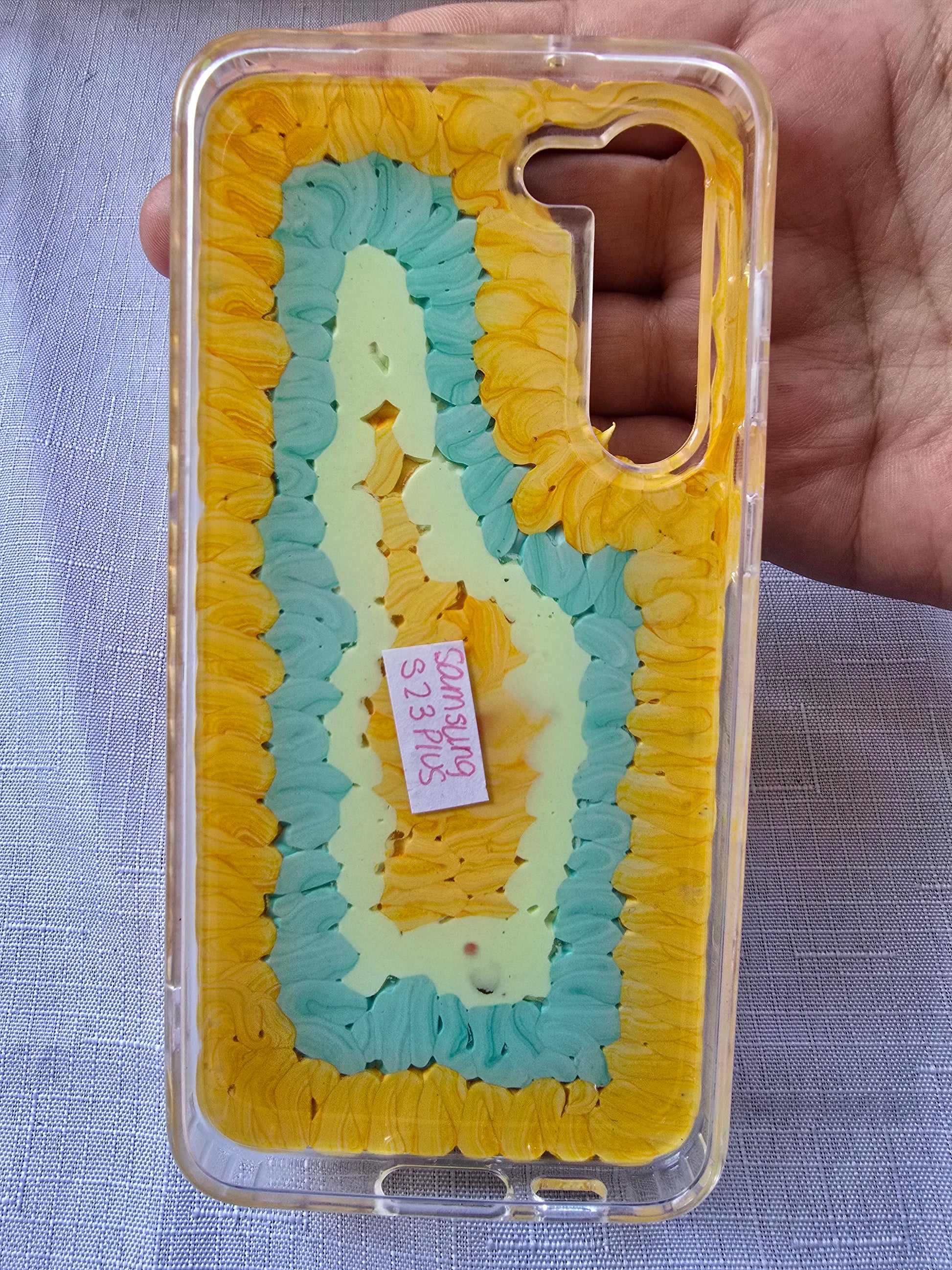 Handmade Samsung S23 Plus phone case with colorful kawaii and toy-themed 3D decorations, featuring a doll figure, pearls, cartoon charms, and candy accents on a yellow base.