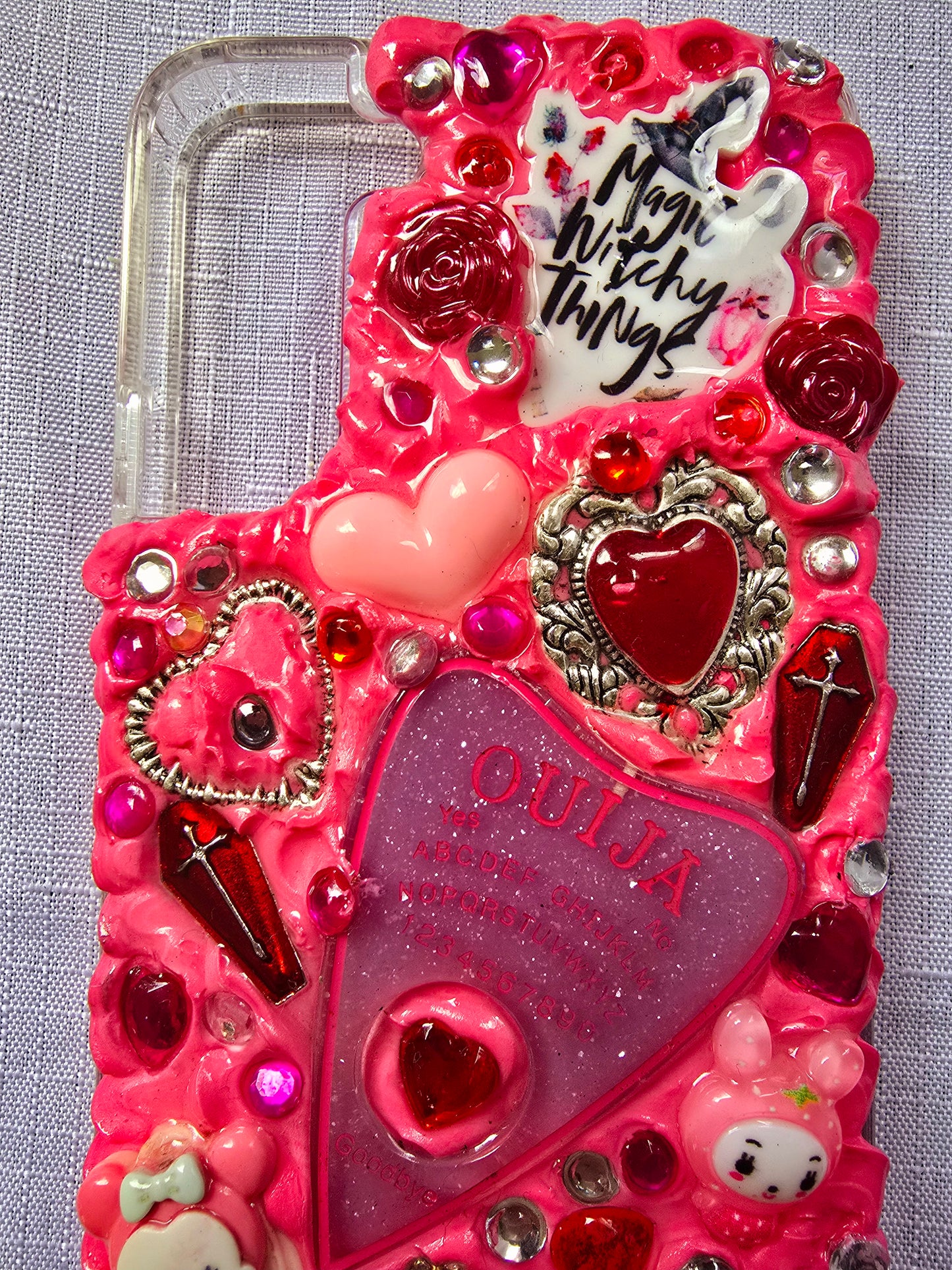 Handmade Samsung S22 Plus phone case with a pink, red, and black witchy kawaii theme, featuring a Ouija planchette, heart charms, My Melody figures, and cute gothic embellishments.