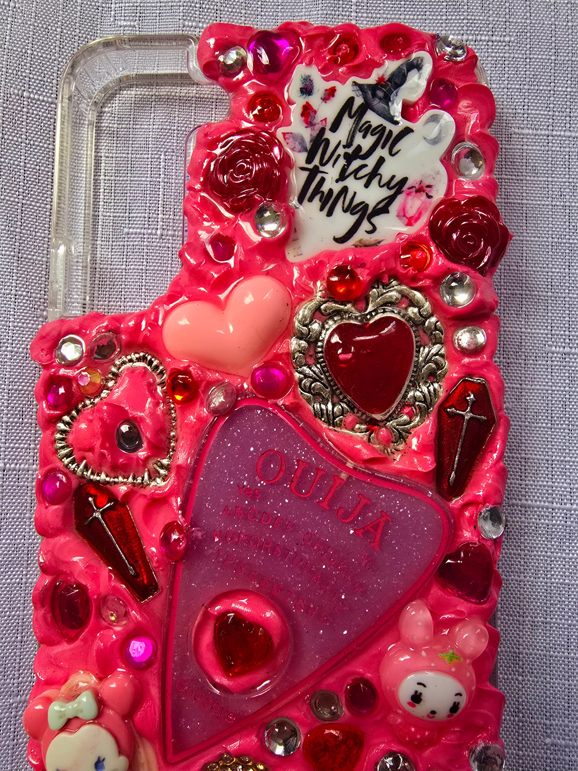 Handmade Samsung S22 Plus phone case with a pink, red, and black witchy kawaii theme, featuring a Ouija planchette, heart charms, My Melody figures, and cute gothic embellishments.