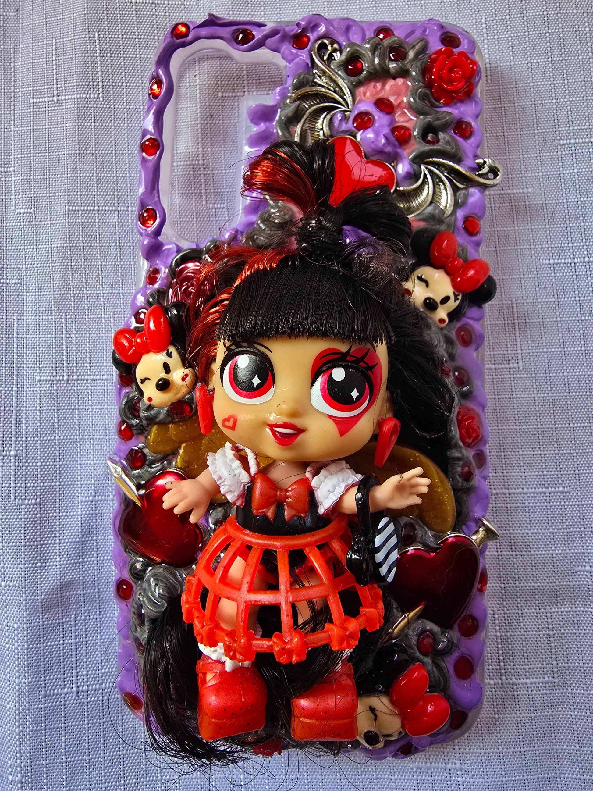 Handmade Samsung S23 Plus phone case with gothic and doll-inspired design, featuring red and black accents, heart charms, and 3D figure on a purple base.