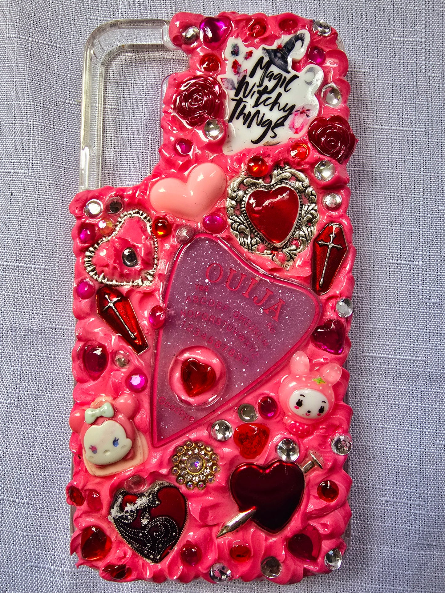 Handmade Samsung S22 Plus phone case with a pink, red, and black witchy kawaii theme, featuring a Ouija planchette, heart charms, My Melody figures, and cute gothic embellishments.