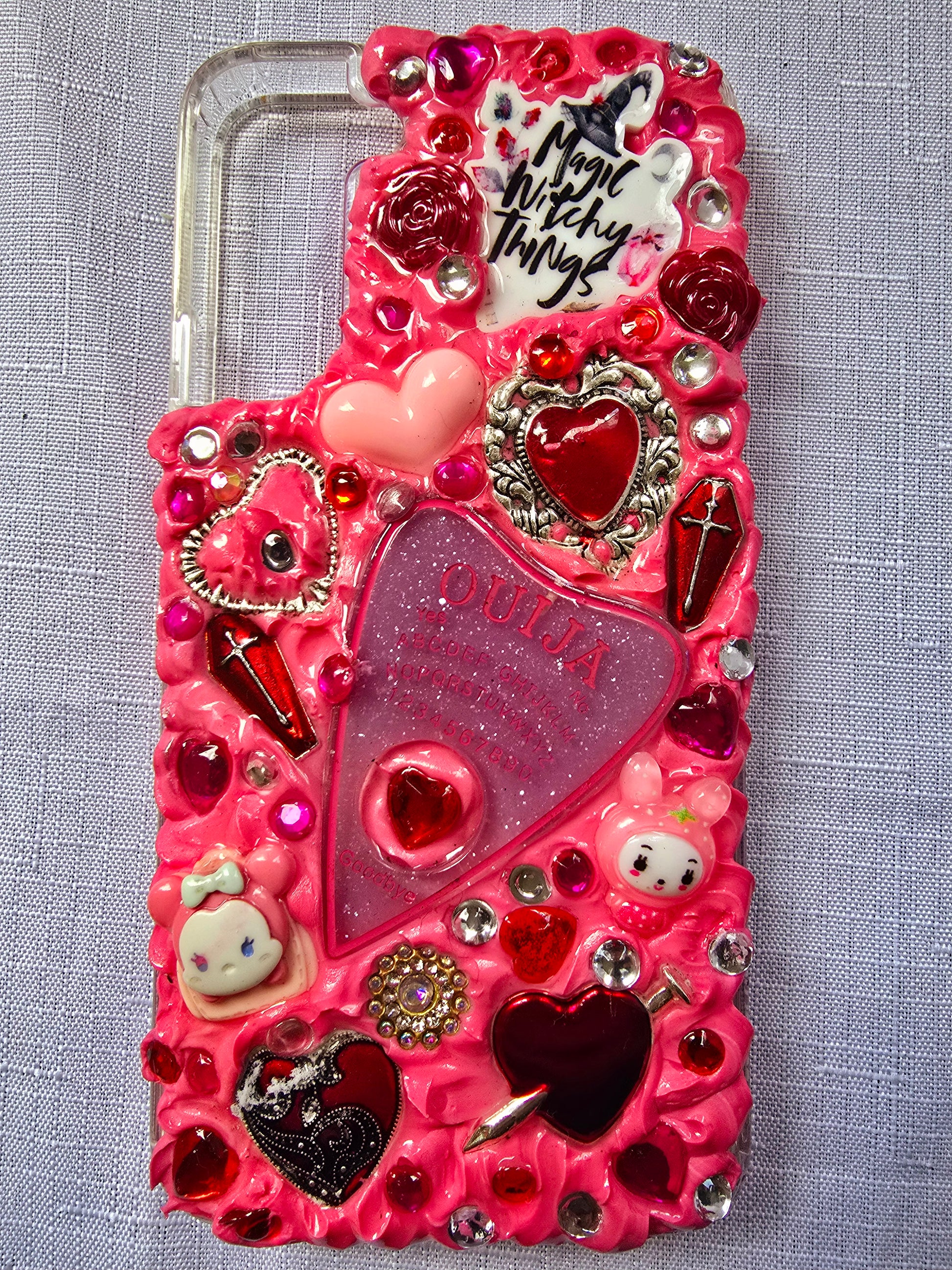 Handmade Samsung S22 Plus phone case with a pink, red, and black witchy kawaii theme, featuring a Ouija planchette, heart charms, My Melody figures, and cute gothic embellishments.